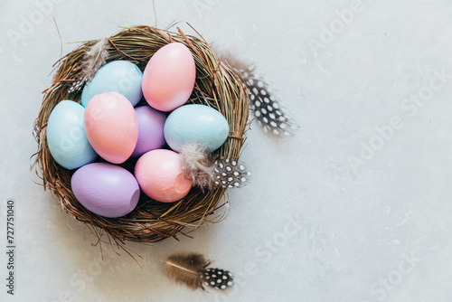 Happy Easter concept. Preparation for holiday. Colorful pastel decorated easter eggs in nest with feather on concrete stone grey background. Simple minimalism flat lay top view copy space