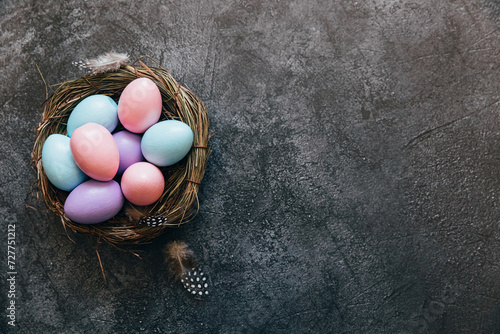 Happy Easter concept. Preparation for holiday. Colorful pastel decorated easter eggs in nest on grunge scratched dark black shale background. Simple minimalism flat lay top view copy space