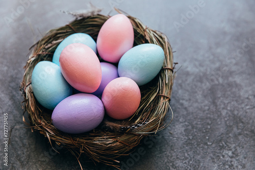 Happy Easter concept. Preparation for holiday. Colorful pastel decorated easter eggs in nest on grunge scratched dark black shale background. Simple minimalism flat lay top view copy space