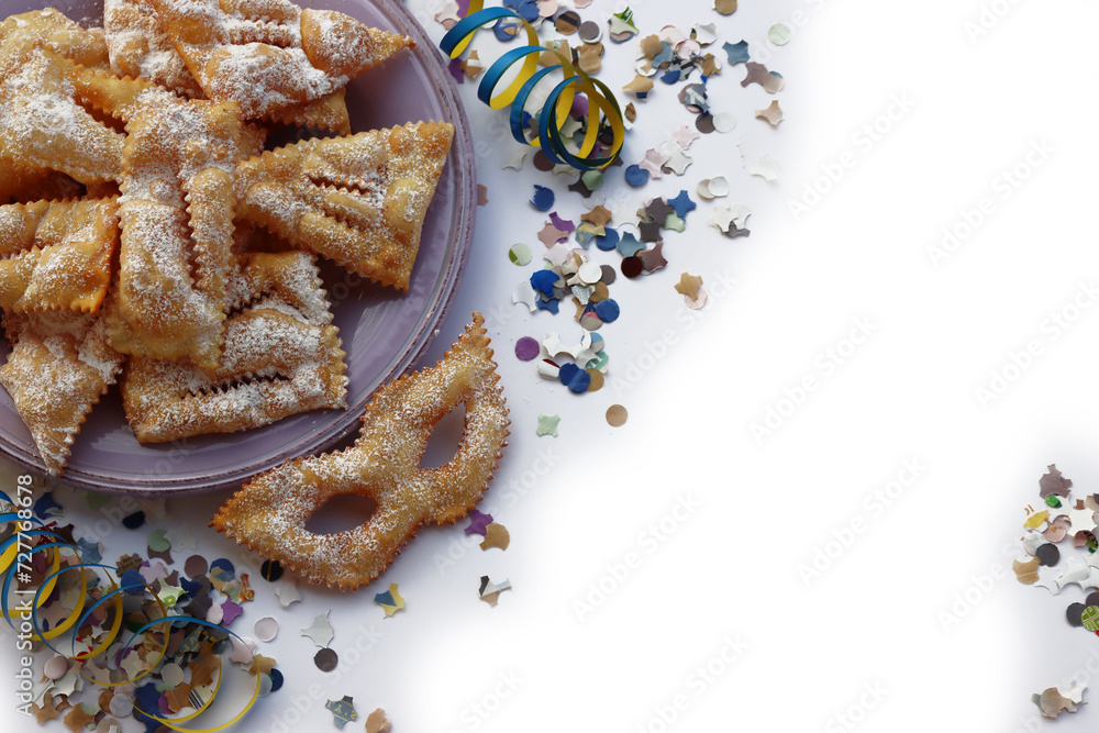 Italian sweet crisp pastry deep-fried and sprinkled with sugar in shape of Carnival mask on colorful plates on white. Chiacchere or crostoli, bugie, cenci with confetti and paper serpentine Italian sweet crisp pastry deep-fried and sprinkled with sugar in shape of Carnival mask on colorful plates on white. Chiacchere or crostoli, bugie, cenci with confetti and paper serpentine