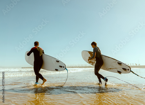 Canvas Print Back view of surfers with surfboards entering towards ocean for surfing on waves