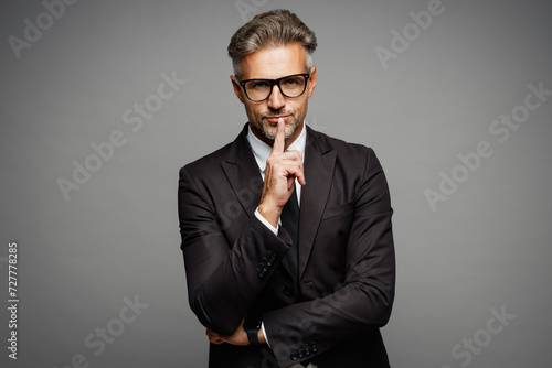Adult successful employee business man corporate lawyer wear classic formal black suit shirt tie work in office say hush be quiet, finger on lips shhh gesture isolated on plain grey background studio.