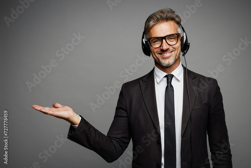 Adult employee operator business man wears black suit set microphone headset for helpline assistance sit work at call center office desk with pc computer isolated on grey background studio portrait.