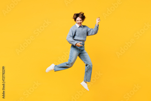 Full body expressive singer virtuoso young woman she wearing grey knitted sweater shirt casual clothes jump high play air guitar isolated on plain yellow background studio portrait. Lifestyle concept.