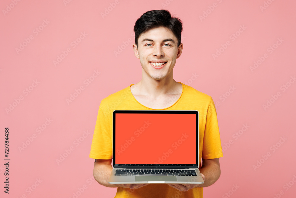 Young IT man wears yellow t-shirt casual clothes hold use work on laptop pc computer with blank screen workspace area isolated on plain pastel light pink background studio portrait. Lifestyle concept. Young IT man wears yellow t-shirt casual clothes hold use work on laptop pc computer with blank screen workspace area isolated on plain pastel light pink background studio portrait. Lifestyle concept.