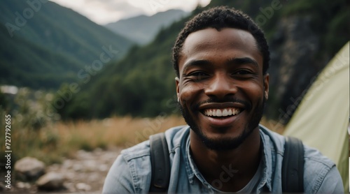 Portrait of a happy smiling handsome young black african man on camping site at the mountain with a tent on the background from Generative AI © Arceli