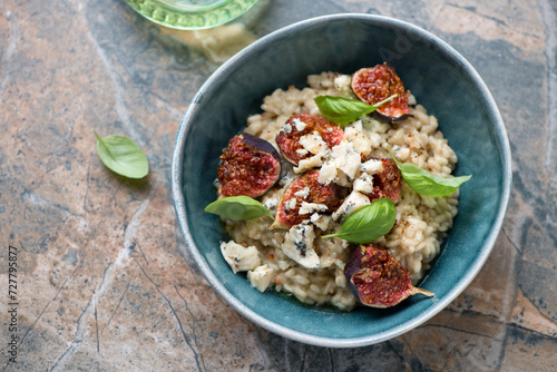Bowl of risotto with fig fruits, blue cheese and fresh basil, horizontal shot on a brown granite background, high angle view