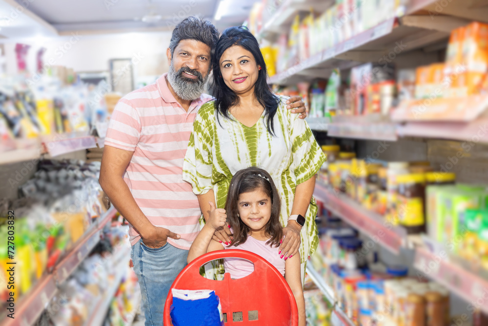 Indian family of three shopping for groceries at the supermarket. Buying grocery for home. Smiling bearded man standing smiling.