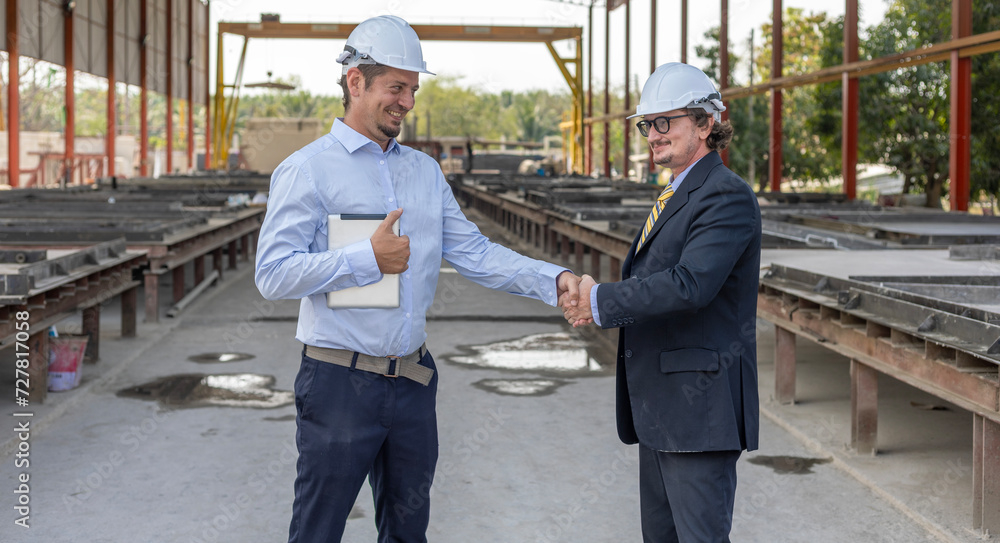 Two civil engineers from different cultures reach partnership agreement and have handshake in a prefabs or floor construction factory Two civil engineers from different cultures reach partnership agreement and have handshake in a prefabs or floor construction factory