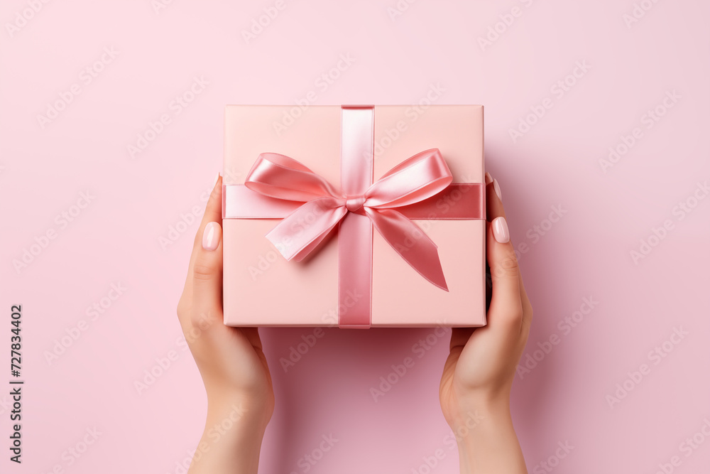 Top view of a female hands holding a pink gift box on pale pink background with copy space Top view of a female hands holding a pink gift box on pale pink background with copy space