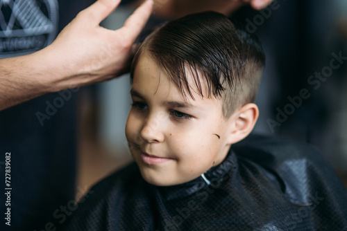 Little Boy Getting Haircut By Barber While Sitting In Chair At Barbershop.