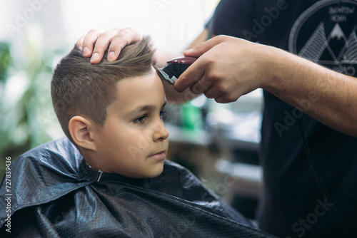 Professional hairdresser uses a hair clipper for fringing hair for a small boy