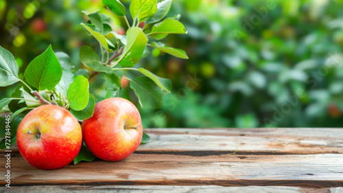 Natural ripe red apples with leaves on empty wooden table for montage against blurred summer orchard background. Template for advertising apple products. Background for presentation of your products