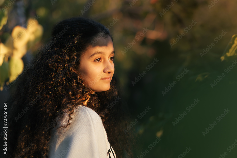 Dreamy scene. A closeup of 13 years old girl watching the sunset through the trees and sunlight touching on her face