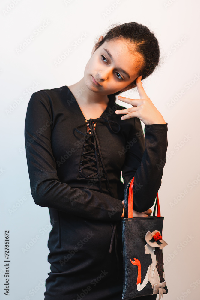 A portrait of fashionable girl in black dress posing in studio for camera and carrying her bag with creative design
