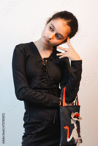 Obraz na płótnie A portrait of fashionable girl in black dress posing in studio for camera and carrying her bag with creative design w salonie