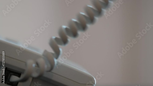 Close-up of a male hand picking up the receiver of a white landline telephone.