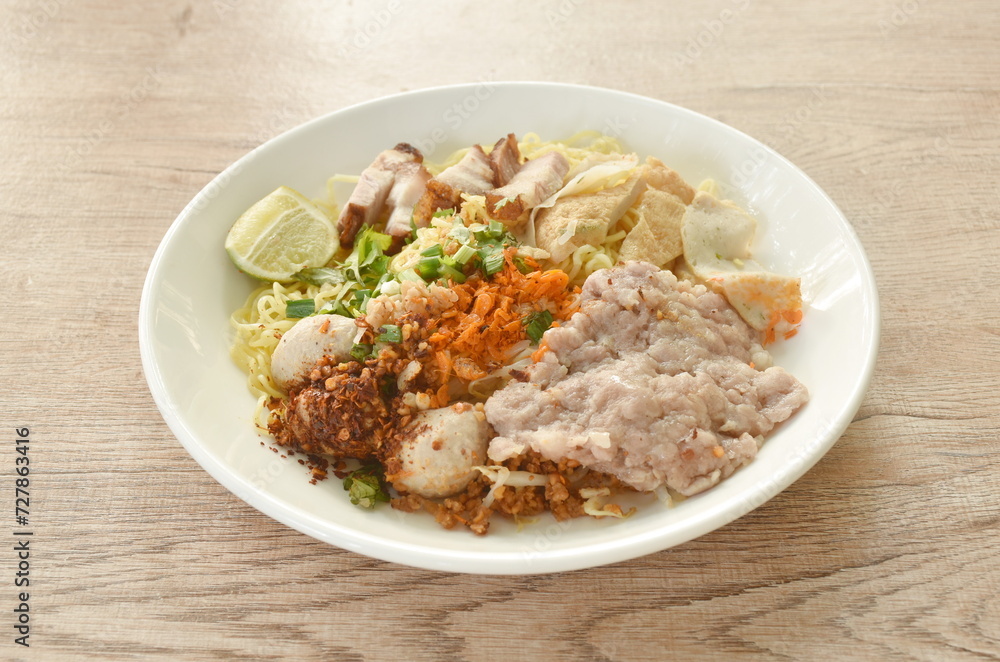 dry Chinese egg yellow noodles topping grilled crispy and boiled chop pork with pork ball dressing cayenne pepper on plate dry Chinese egg yellow noodles topping grilled crispy and boiled chop pork with pork ball dressing cayenne pepper on plate