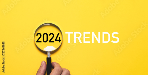 Hand holding magnifier glass with 2024 trends for marketing monitor and business focus planing in new year concept.