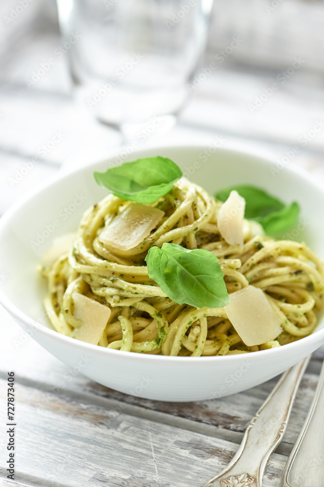 Spaghetti with olive pesto sauce and fresh basil. Bright wooden background. Close up	