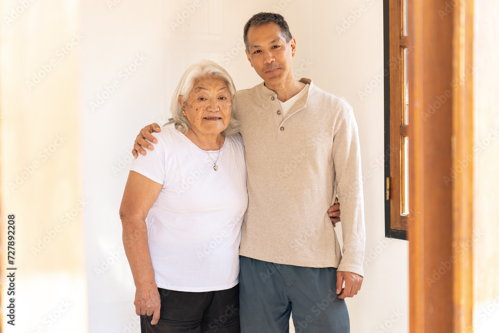 Japanese-born mother and son stand smiling embraced looking at camera. Japanese-born mother and son stand smiling embraced looking at camera.
