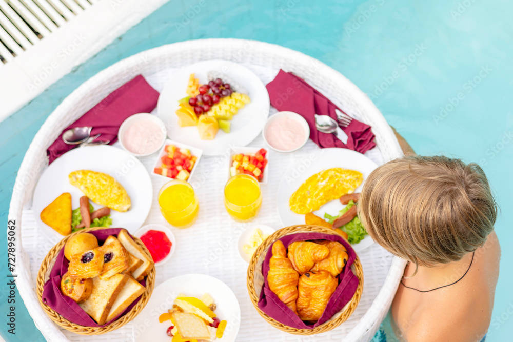 Obraz premium teenage boy with served floating tray in swimming pool with drinks and snacks on tropical island resort in Maldives, breakfast for romantic date or honeymoon in luxury hotel, travel concept