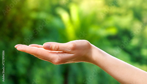 Side close-up of a hand of a white person, palm up to present something for product presentation and product advertising. Green plants in the background © Marcus Jacobi