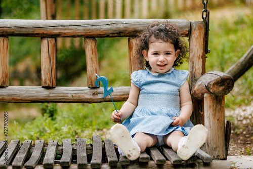 Happy two years old toddler girl with curly hair girl sitting on the bench and holding her birthday number candle