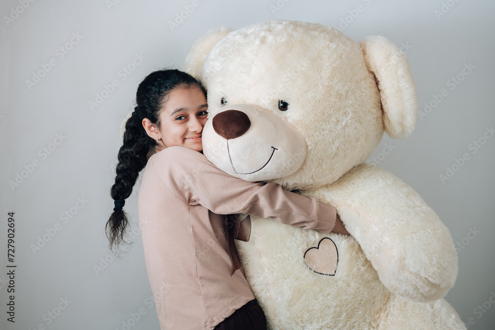 Studio shot of 13 years old cheerful girl with lots of emotions raising her teddy and having fun