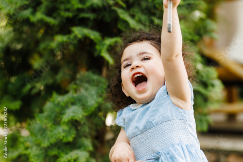 Obraz na płótnie Very happy little joyful girl full of positive emotions in front of the green tree in the garden w salonie
