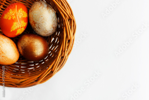 Four Easter eggs painted in different shades of brown color lying in a wicker basket on white background. Simple Easter flat lay in neutral colors with copy space