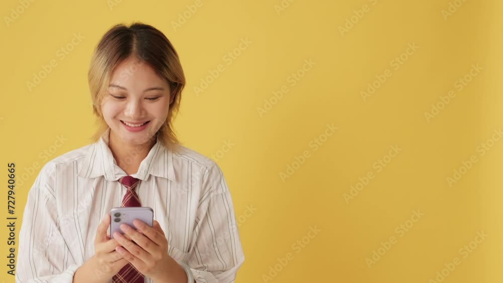 Smiling young woman using mobile phone isolated on yellow background in studio Smiling young woman using mobile phone isolated on yellow background in studio