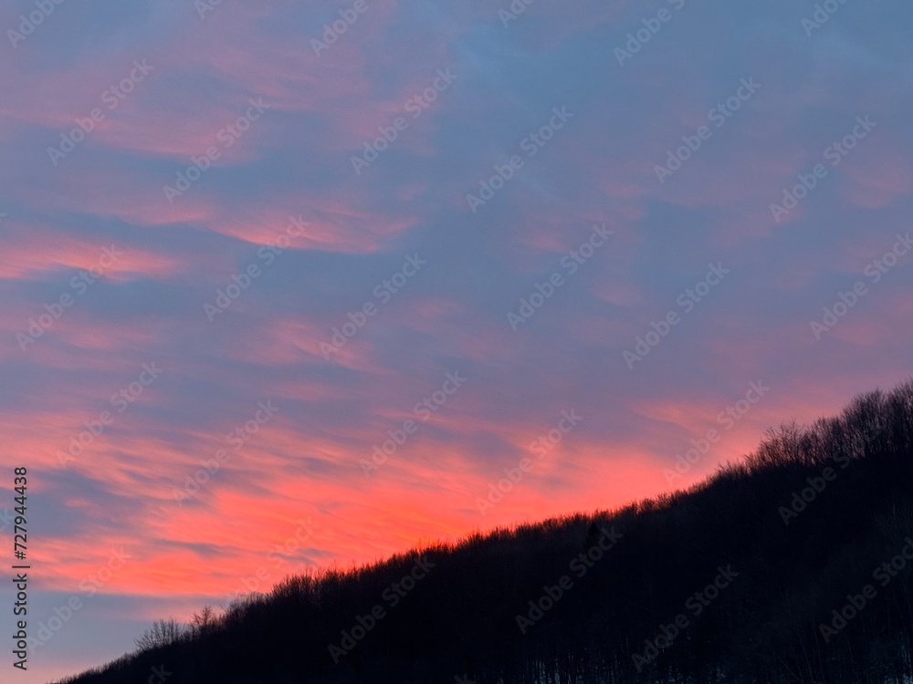Fototapeta premium Orange sunset in cloudy sky over dark mountain forest