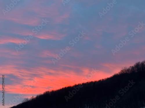 Orange sunset in cloudy sky over dark mountain forest