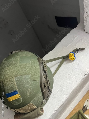 High angle view of military helmet with ukrainian flag and yellow and blue bracelet on old white windowsill. Russo-Ukrainian War
