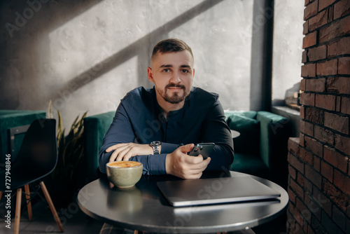 A young guy with a beard sits with a phone and monitors the crypto market. Free lance in the cafe photo