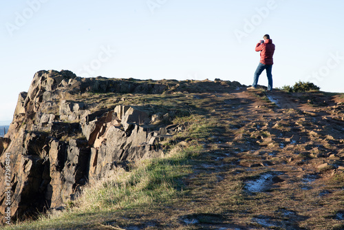 A beautiful view of a person over a top of a high mountain on Salisbury Crags looking to a cityscape. Destinations in Europe  Space for text  Selective focus.