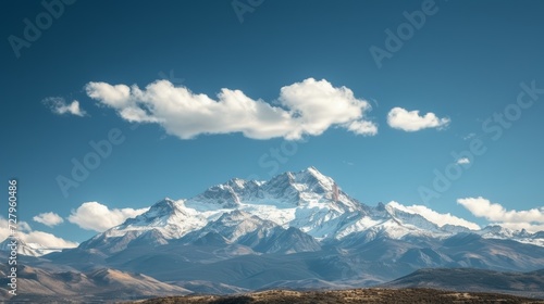 Majestic mountains capped with snow  under a clear blue sky with soft  white clouds.