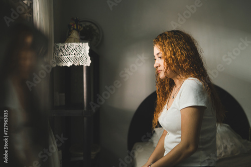Side view of a sad woman sitting on the bed.