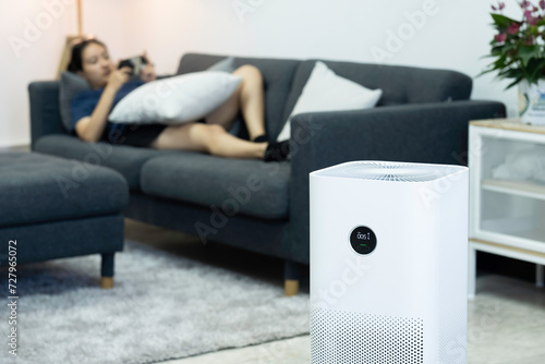 Air purifier, PM 2.5 dust filter, clean and health air. Air purifier against blurred woman using the phone on sofa in living room. .