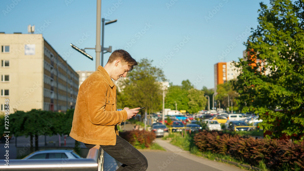 Teenager sitting with phone in sunshine in a city - Stock photo