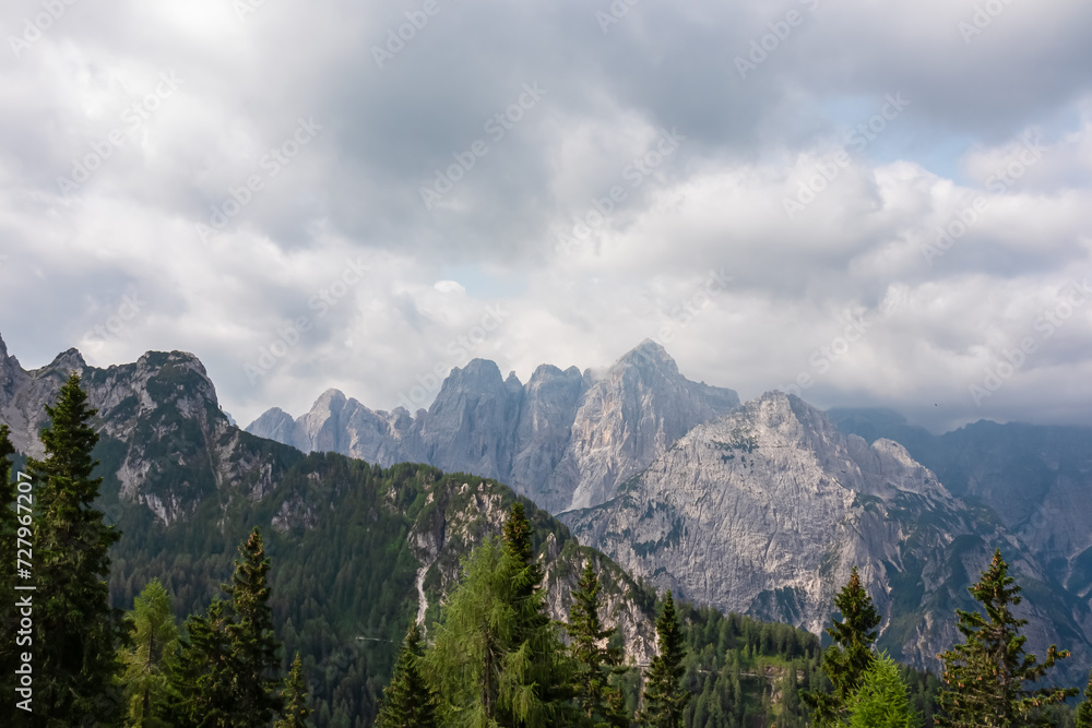 Panoramic view from Monte Lussari in Camporosso, Friuli Venezia Giulia, Italy. Looking at majestic mountain peaks of Julian Alps. Massive rock ridges of Jof Fuart, Cima di Riofreddo covered by clouds