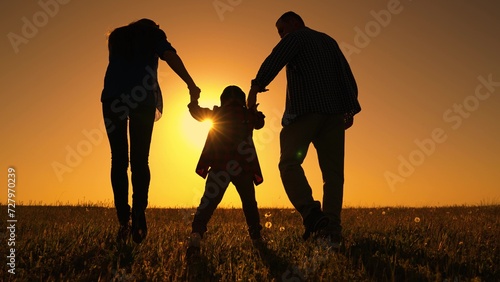 Family walk in spring. Happy family dad mom child go walk in meadow, kid holding parents hands on sunny day. Father mother child play together in nature. Little daughter family play in park. Childhood