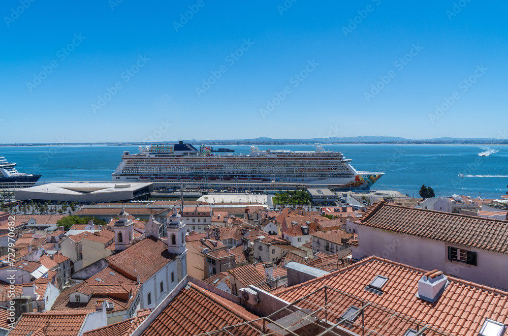 Top view from Lisbon's Alfama neighborhood of a large cruise ship docked in the port, with pleasure boats and yachts sailing around.