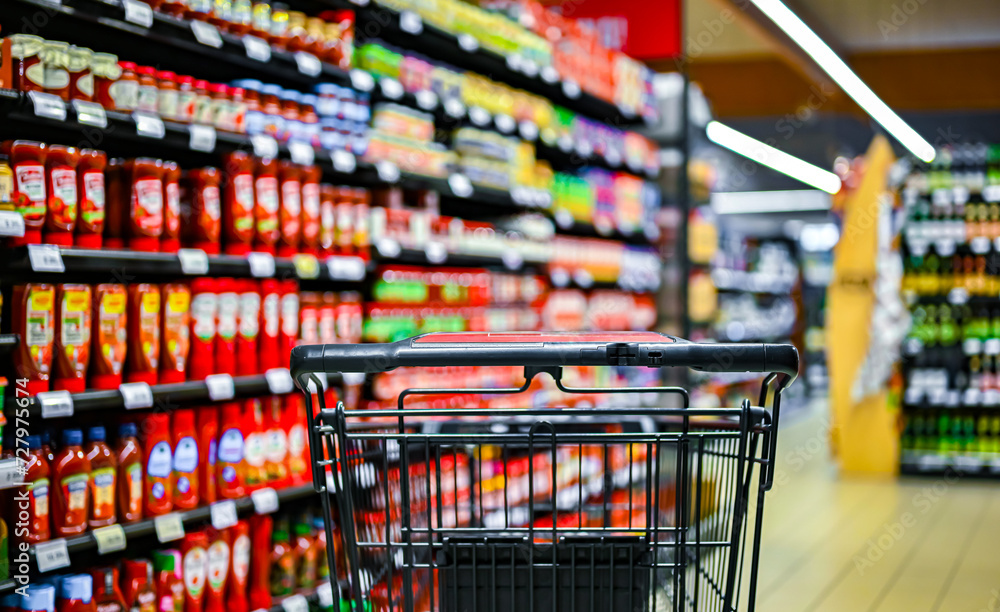 A shopping cart by a store shelf in a supermarket A shopping cart by a store shelf in a supermarket