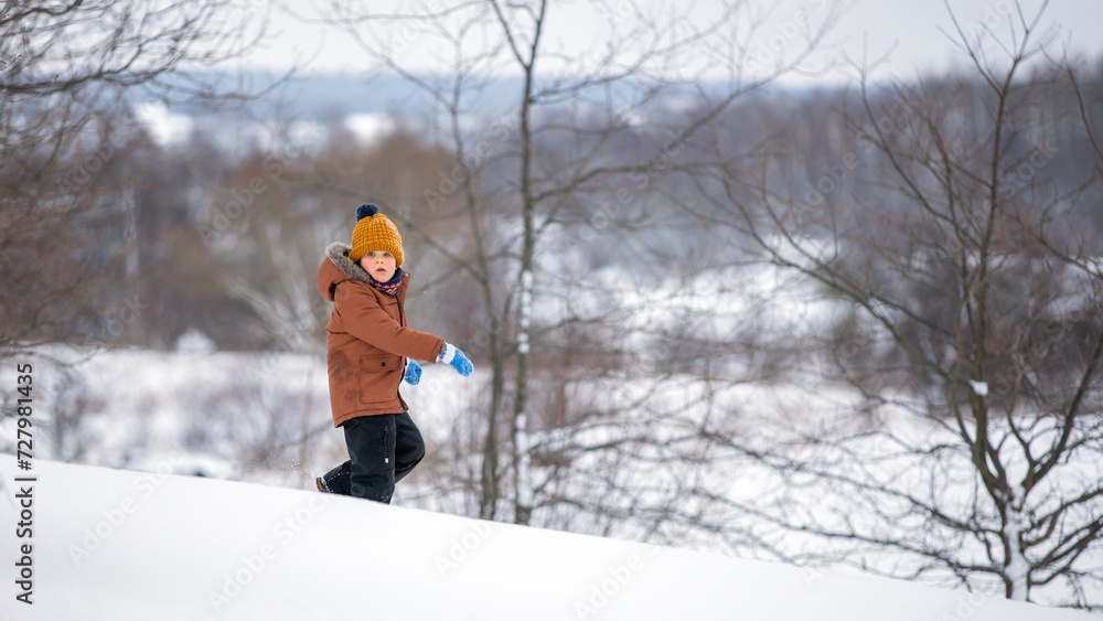 Cute little brave boy running down the snow mountain on a beautiful winter nature background