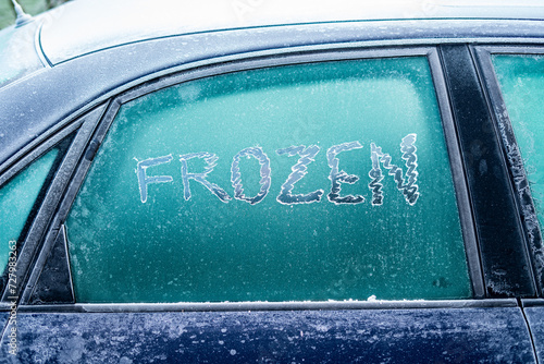 A frozen car window with the word FROZEN written in ice by scraping the ice with your fingers