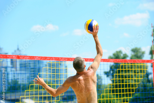 Beach volleyball. Young man volley player hitting over the net attacking