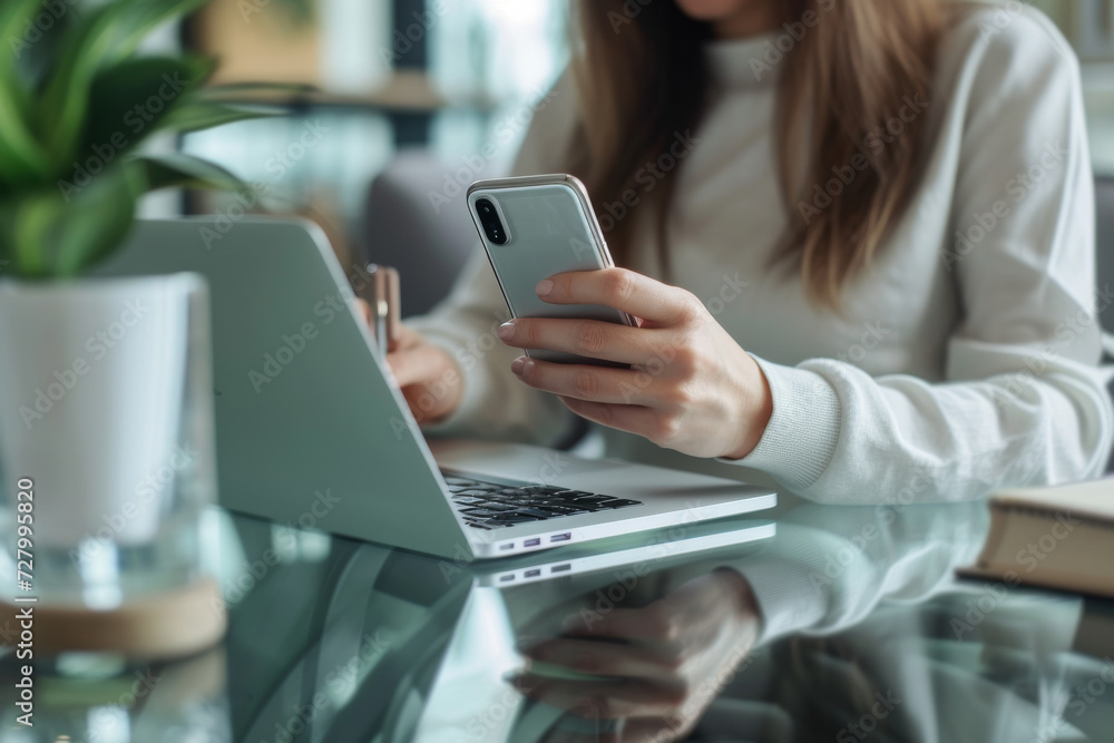 A woman is using a laptop and a cell phone