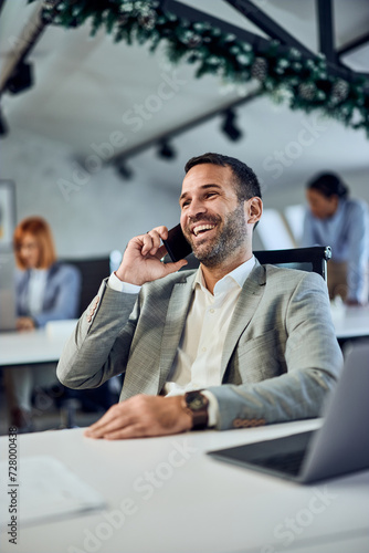 A smiling businessman having a phone call, taking a break from work at the co-working space. Colleagues in the background.